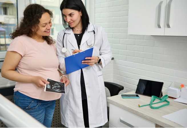 Pregnant woman and doctor in a clinic reviewing an ultrasound image together, clipboard in hand.