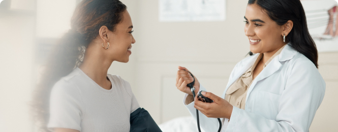 hera-benefits-img (5) Healthcare professional checks a patient's blood pressure using a cuff and stethoscope in a clinic, both smiling at each other.